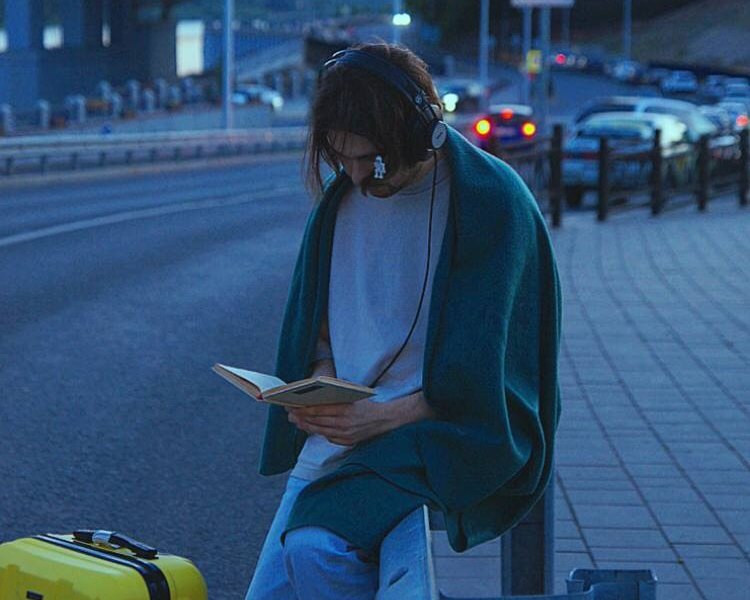 С книгой и в наушниках у дороги, с жёлтым чемоданом